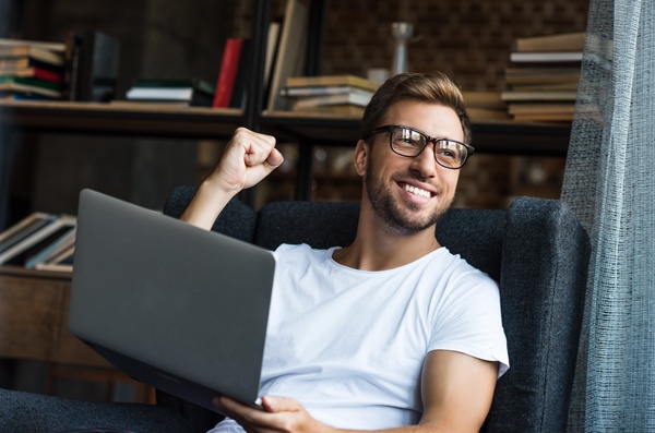 Man with laptop celebrates finding the resource he needs. 