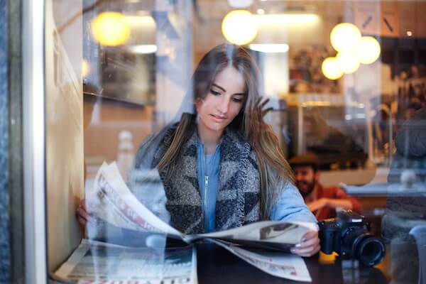 A woman reads a newspaper in a cafe. Photo by Keenan Constance — https://unsplash.com/photos/F7n6gixbJK0