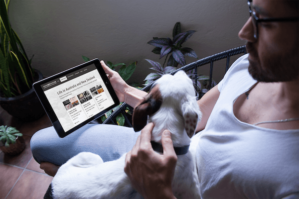 A man checks out the Anzac Sights and Sounds website with an iPad in his hand and a dog on his lap.